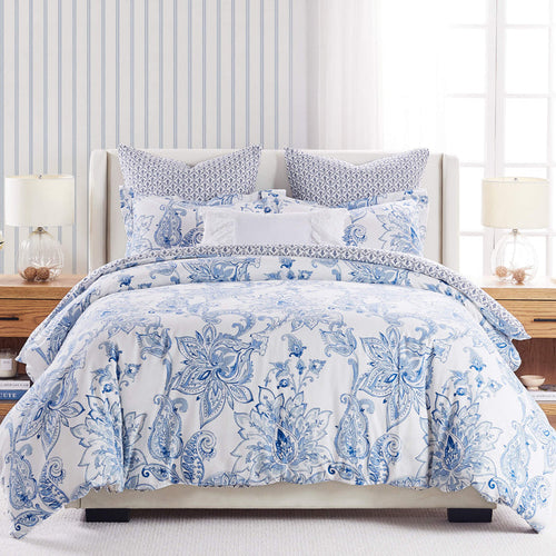 Blue and white floral king comforter set with patterned pillows on a neatly made bed in a bright, coastal-style bedroom.
