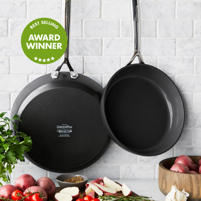 Two ceramic nonstick frypans, 9.5 and 11, hang on a tiled wall with an award badge above fresh vegetables below.