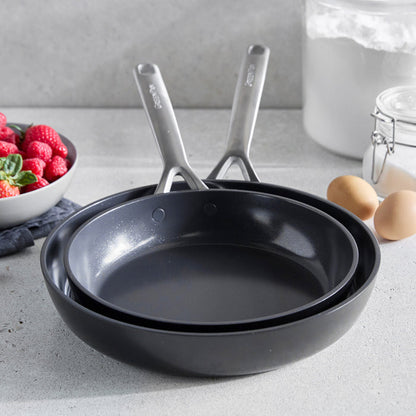 Two ceramic nonstick frypans, 9.5 and 11, stacked on a counter with eggs, strawberries, and flour nearby.