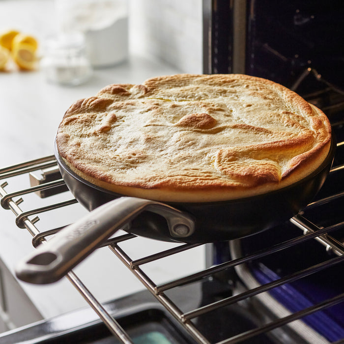 Golden Dutch baby pancake in a ceramic nonstick frypan from a set on an oven rack in a modern kitchen.