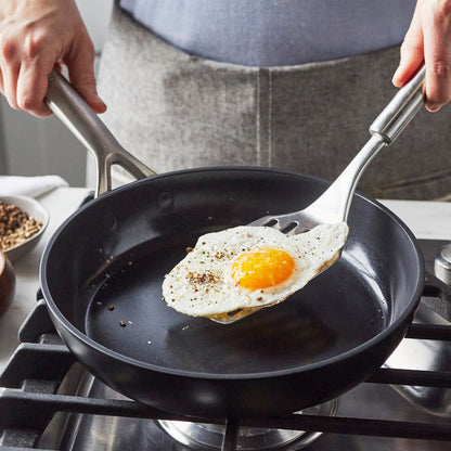 Sunny-side-up egg lifted from a set of two GP5 Infinite8 ceramic nonstick frypans with a spatula.