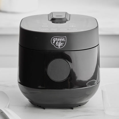 Black 4-cup rice and grains cooker on a white countertop with a spatula and clear measuring cup beside it.