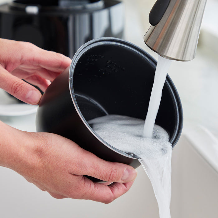 Black GreenLife 4-cup rice and grains cooker being washed with soap under running water in a sink.