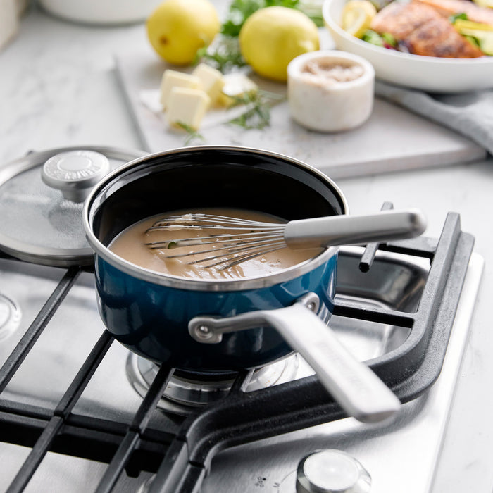 Whisk stirring gravy in a teal enameled steel 1.5-quart saucepan with lid on a stovetop.