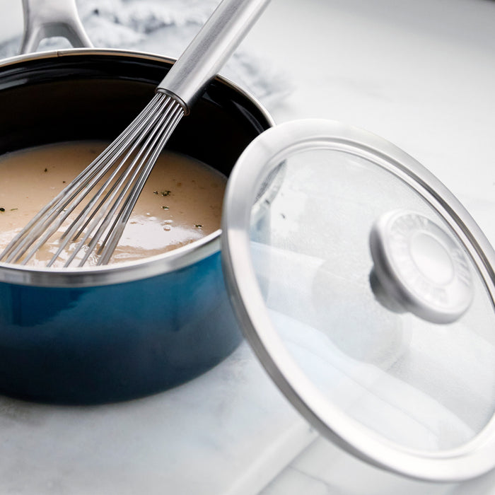 A whisk stirs sauce in a Merten  Storck Aegean Teal Steel Core 1.5-Qt Saucepan on a white countertop.