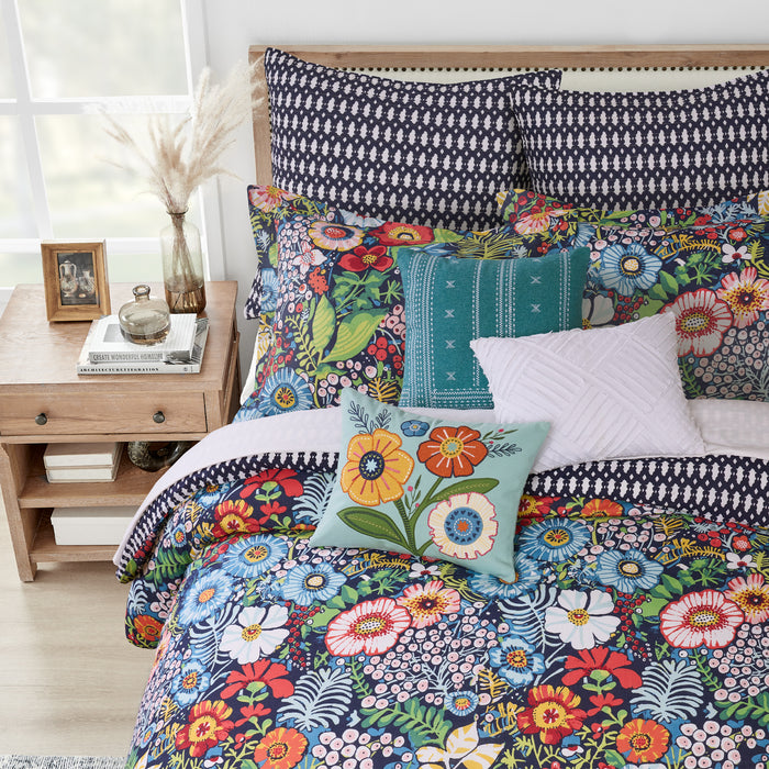 Colorful floral bedding set on a bed with a wooden nightstand in the background.