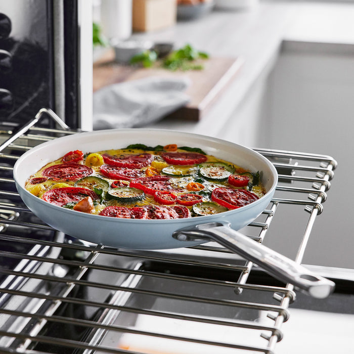 Tomato and zucchini frittata cooking in a white ceramic nonstick frypan set on an oven rack.