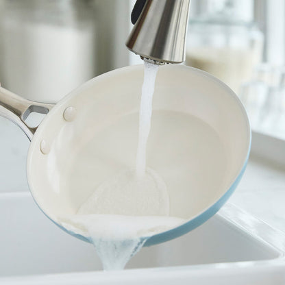 Two blue ceramic nonstick frypans, 8 and 10, being rinsed under running water in a kitchen sink.
