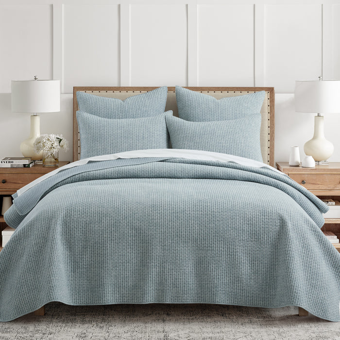 Blue checkered quilt and pillow set on a bed in a bedroom setting.