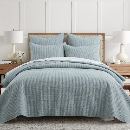 Blue checkered quilt and pillow set on a bed in a bedroom setting.