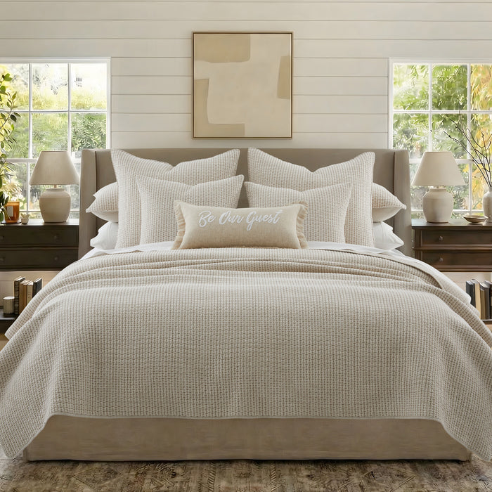 Neatly made bed with beige bedding and pillows in a well-lit bedroom.