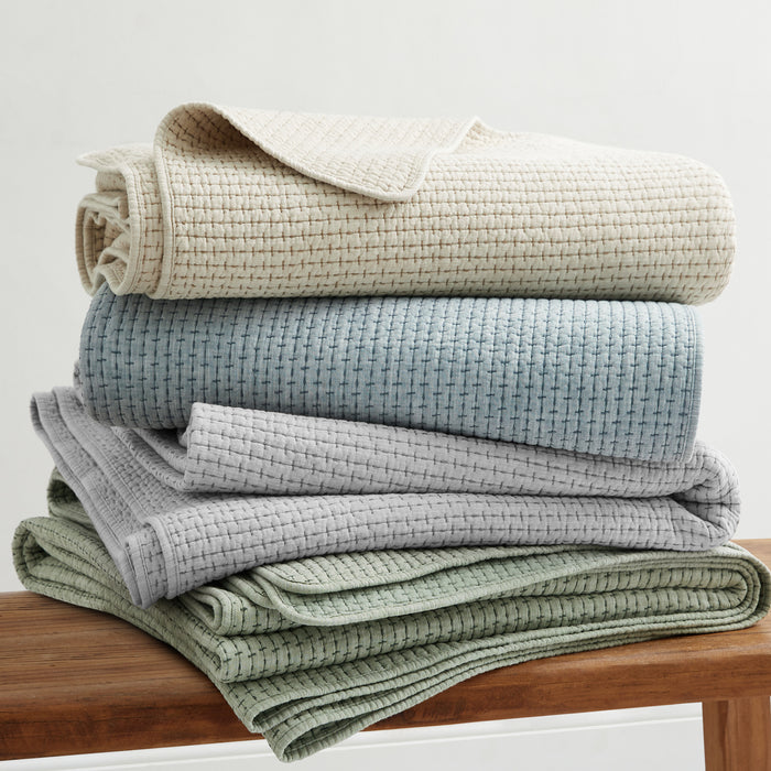 Pick-Stitch Artisan Quilted Throw in soft, textured fabrics stacked on a wooden surface.