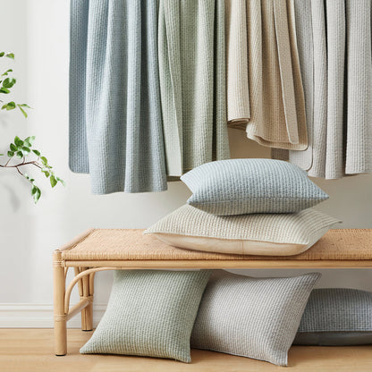 Pick-Stitch Artisan Square Pillow in various colors on a woven bench, showcasing relaxing artisan textures.