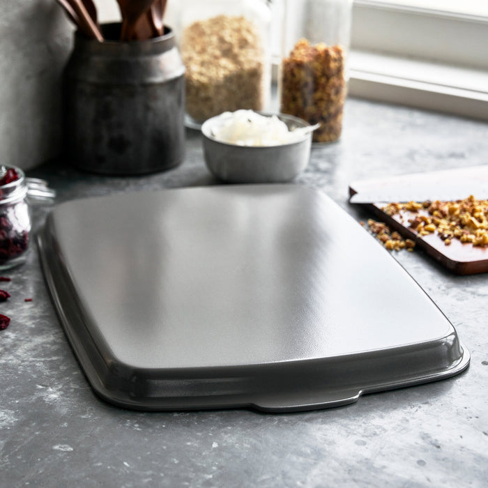 Gray ceramic nonstick half sheet pan on a countertop with bowls and chopped nuts nearby.