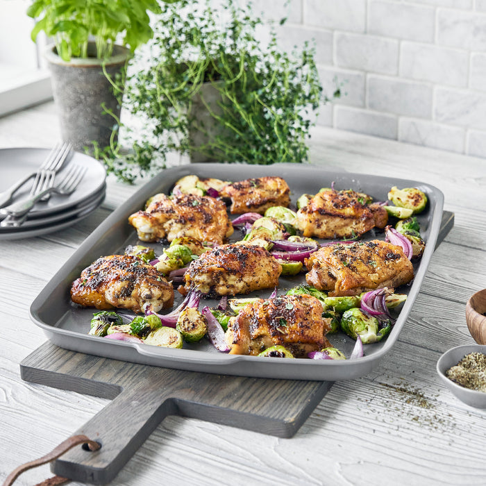Chicken thighs, Brussels sprouts, and red onions on a rectangular white ceramic nonstick half sheet pan.