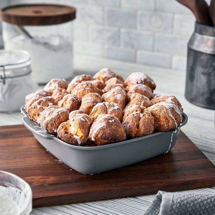 Gray ceramic nonstick square baker with glazed monkey bread inside, topped with powdered sugar.