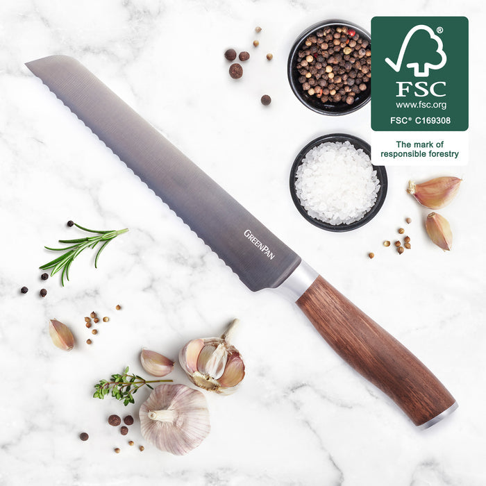 Bread knife with walnut handle on marble, surrounded by herbs, garlic cloves, salt, peppercorns, and FSC logo.