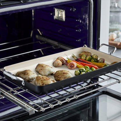 Chicken thighs and vegetables roasting on a black Rio Double Griddle with high walls and steel handles.