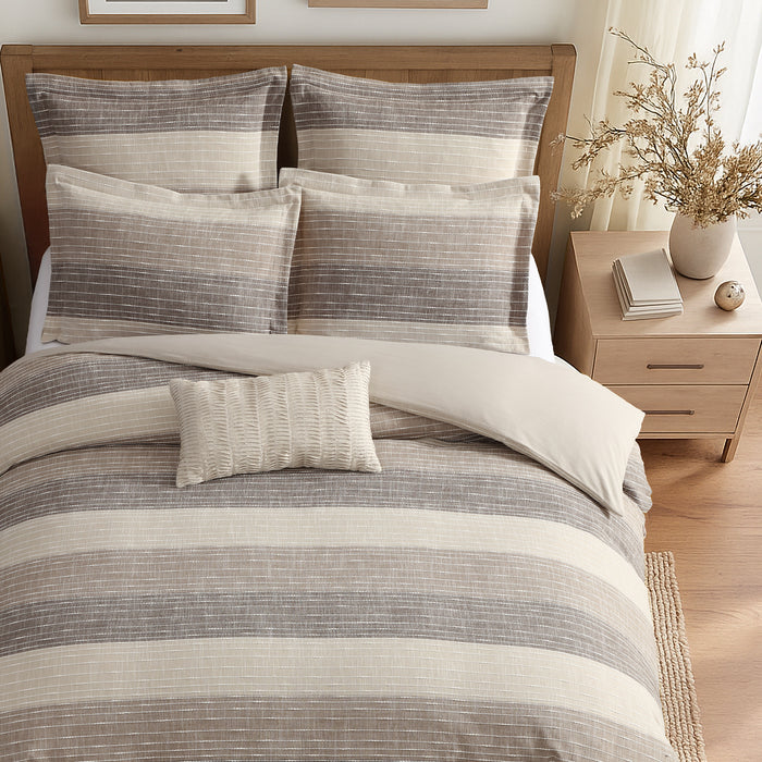 Striped bedding set on a bed with a wooden headboard and side table in a bedroom setting.