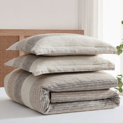 Stack of striped bedding and pillows on a bed with a light background