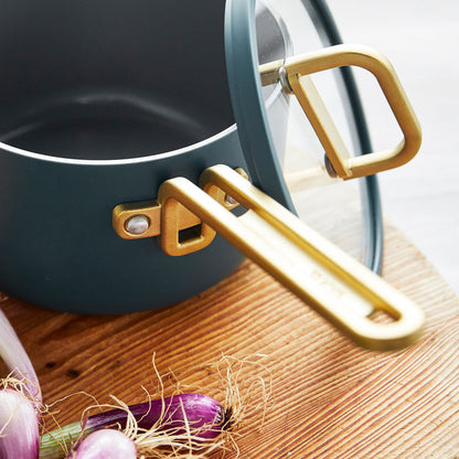 Venetian teal saucepan with gold handle and lid next to fresh shallots on a kitchen surface.