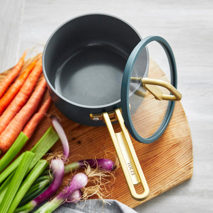 Ceramic nonstick 2-quart teal saucepan with lid next to fresh carrots, onions, and celery.