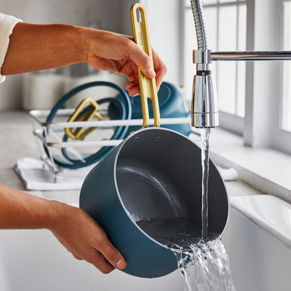 Washing a teal ceramic nonstick saucepan at the sink, with other pots air drying nearby.