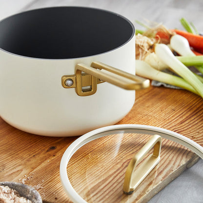 White ceramic 4-quart saucepan with lid, surrounded by assorted fresh vegetables on a wooden board.