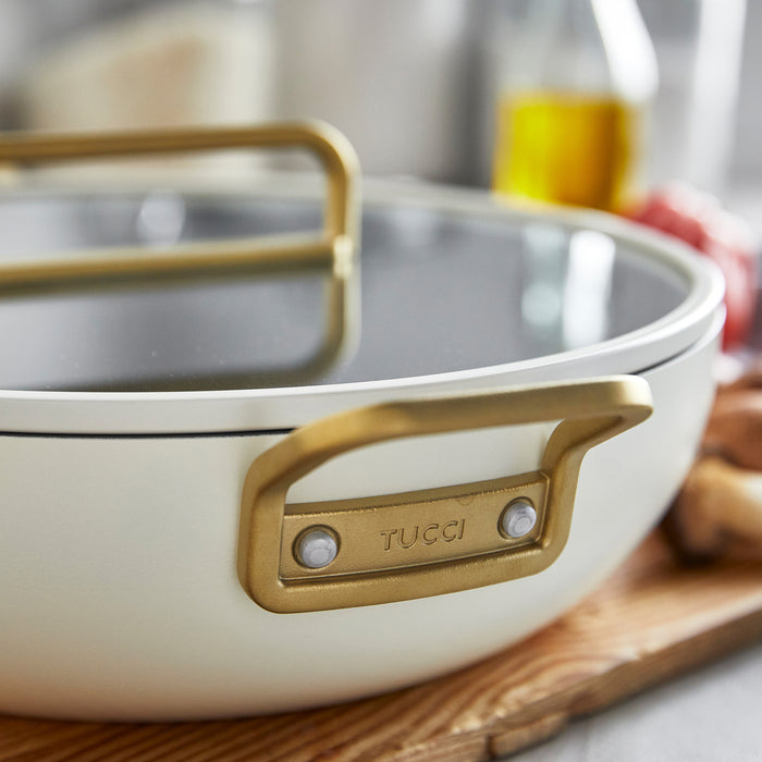 White ceramic nonstick pan with gold handle and lid, 6.5-quart size, resting on a board.