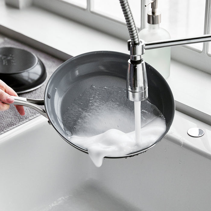 Hand washing a soapy 8-inch Swift ceramic nonstick frypan under running water in a kitchen sink.