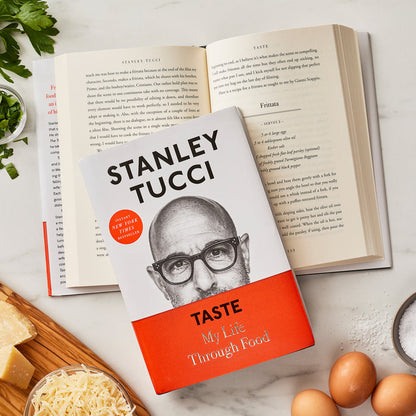 Stanley Tuccis Taste: My Life Through Food cookbook on a table with Italian recipes and an open book in the background.