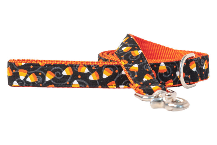 Halloween-themed dog leash featuring colorful candy corn scattered over a black fabric with swirling details and dots. The bright nylon webbing lining adds extra seasonal flair, while the strong hardware ensures secure use during trick-or-treat strolls.