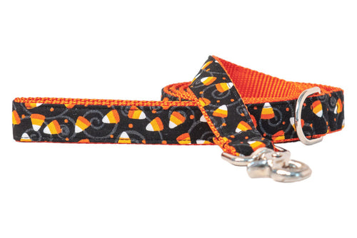 Halloween-themed dog leash featuring colorful candy corn scattered over a black fabric with swirling details and dots. The bright nylon webbing lining adds extra seasonal flair, while the strong hardware ensures secure use during trick-or-treat strolls.