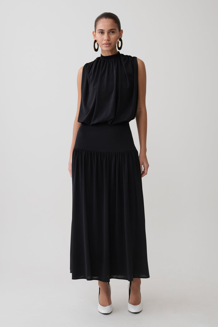 Woman wearing a black sleeveless drop waist gathered midaxi dress.